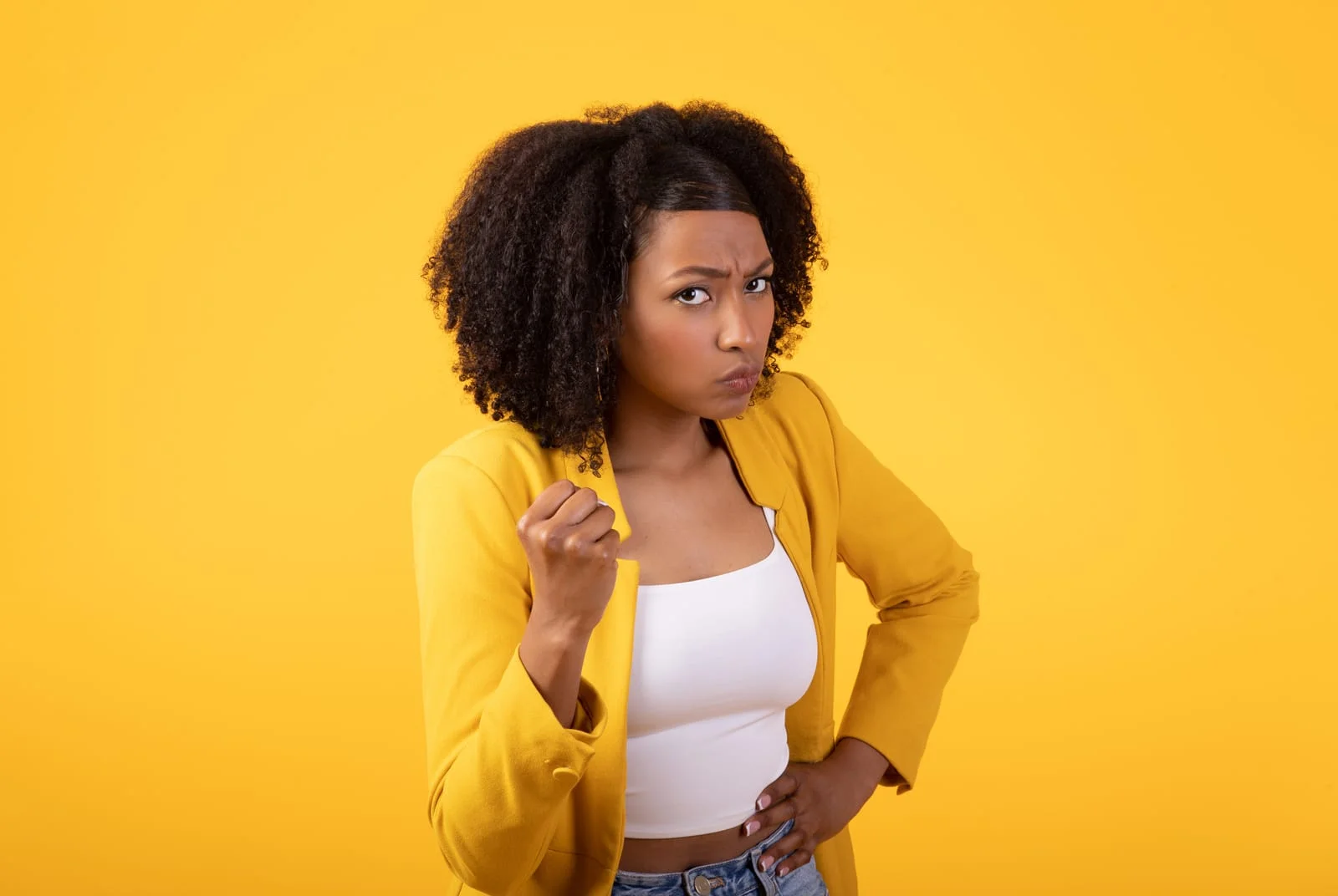 displeased angry black young woman clenching fist looking with aggression at camera over yellow studio background